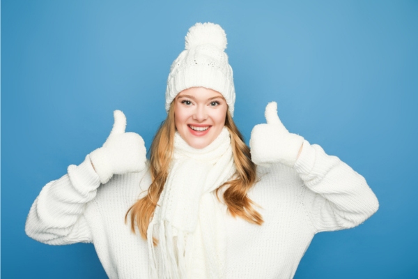 woman in all white winter outfit holding two thumbs up depicting advantages of heating oil