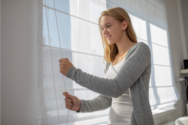 young woman lowering interior blinds to keep warm