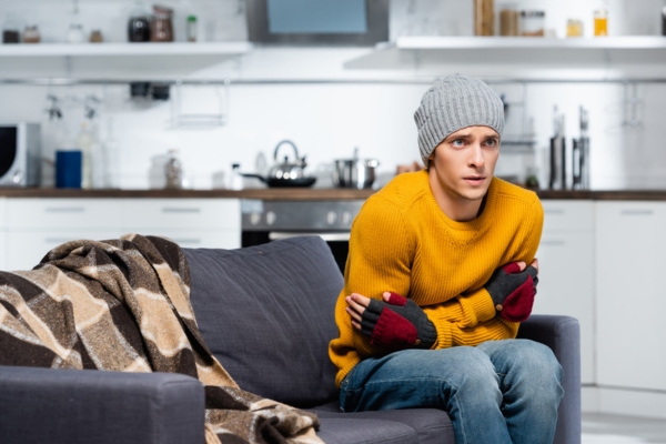 Man in warm hat and fingerless gloves hugging himself depicting heat pump not working properly