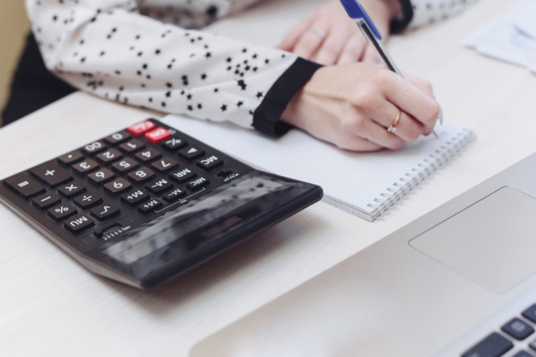 cropped view of a woman's hand computing and writing on a notebook depicting heating oil consumption assessment