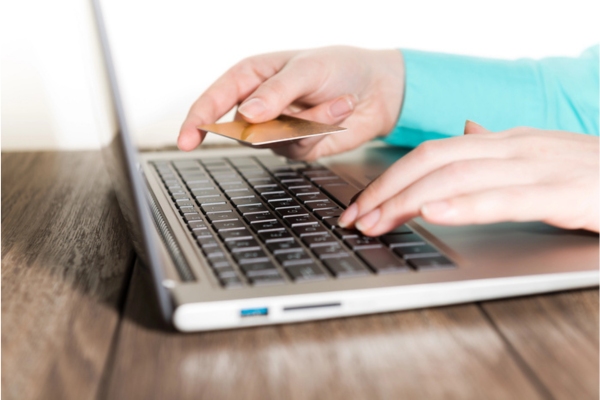 Hands holding a credit card and using laptop computer for automatic oil delivery