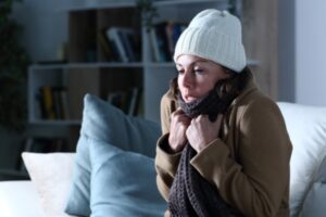 Cold adult woman covered with clothes freezing sitting on the couch depicting heating emergency