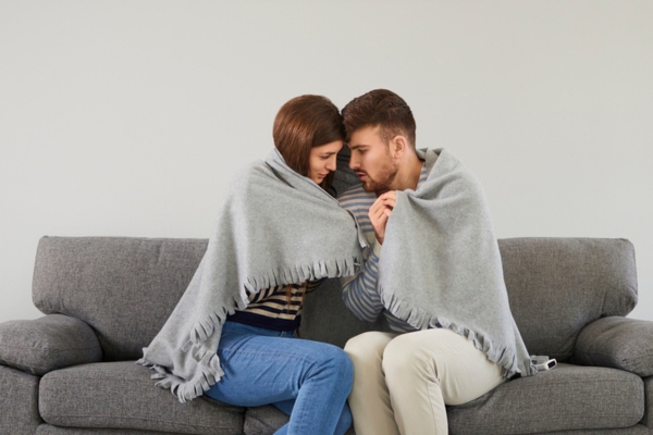 couple sharing a throw blanket due to cold home in winter