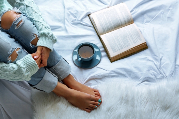 cropped view of a woman reading a book while having tea and staying cozy indoors during winter