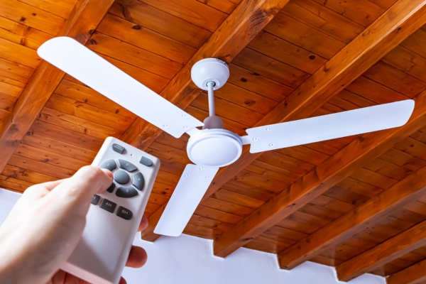 homeowner uses a remote control to turn on a white ceiling fan